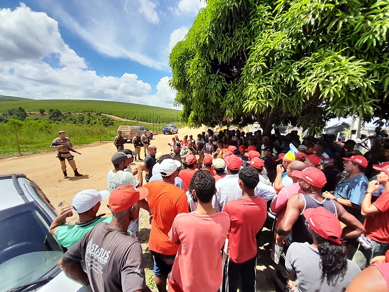 A crowd of people gather in a rural area facing several armed men dressed in uniform